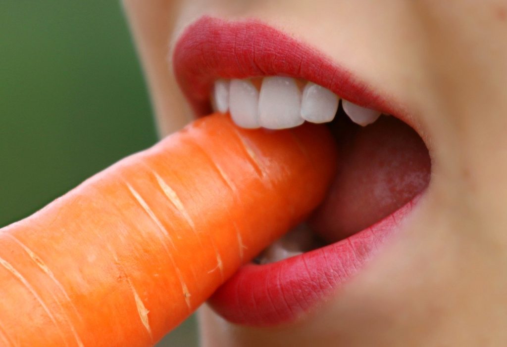 Biting and eating Person biting into a carrot