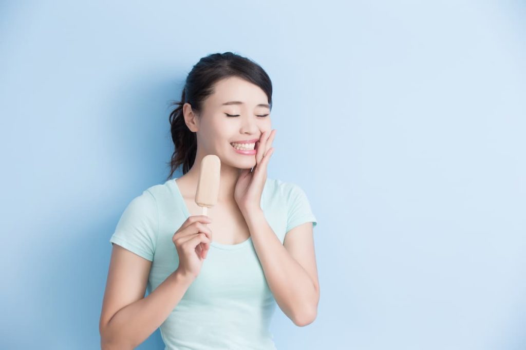 woman have sensitive teeth with ice isolated on blue background.