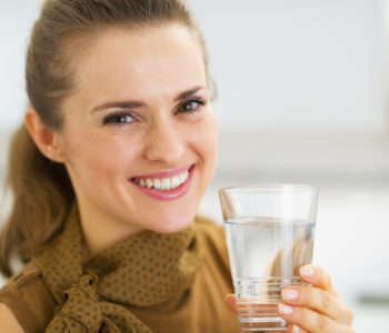 Portrait of happy young woman drinking water in kitchen
