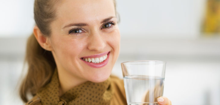 Portrait of happy young woman drinking water in kitchen